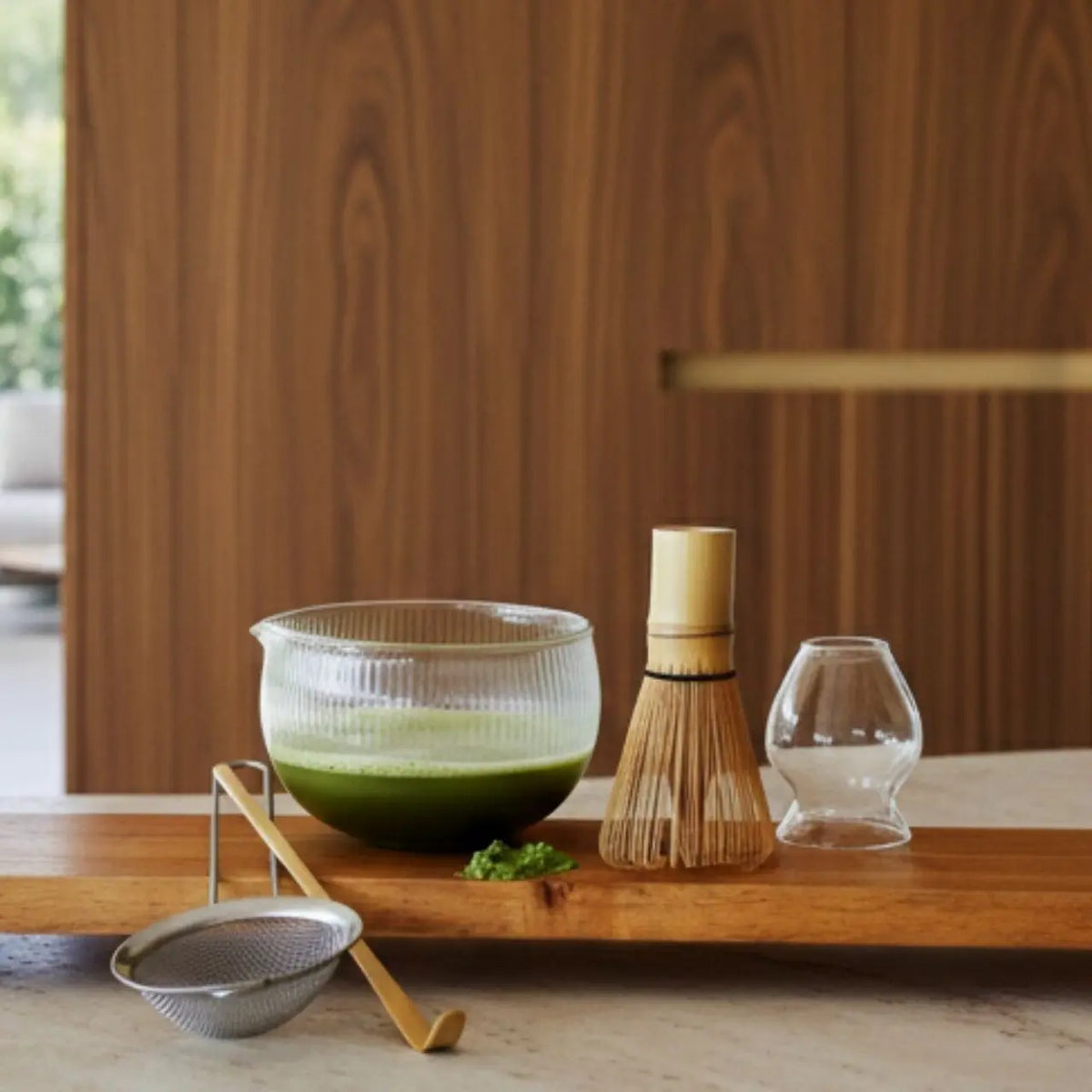 Opgeklopte matcha in de glazen kom naast de bamboe garde en de zeef