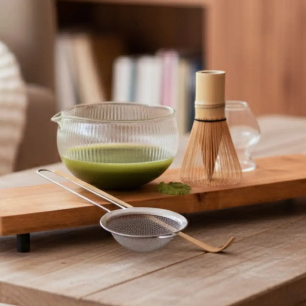 Matcha in een glazen kom met bamboe garde, zeef en lepel op een plank