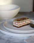 Stuk gelaagde taart op een wit dessertbord met een witte kom erachter