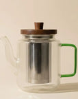 Glazen theepot met jadegroen handvat op een lichte achtergrond